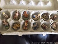 Top-down photo showing 12 small tea-themed figurines each in an individual compartment of an egg carton tray. Figurines include characters, animals, and tea-related items like a teapot and clock.