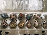 Photo of a set of twelve assorted ceramic figurines arranged in a cardboard egg carton, from which five are claimed as part of the lot.