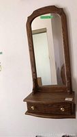 Front view of wall mounted mirror with wooden frame showing arched top and single drawer with brass knobs below.