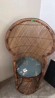 Front view of the wicker fan-style chair with visible blue floral cushion, showing the high fan back and detailed wickerwork around seat and base.