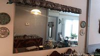 Clear image showing the mirror mounted on wall with reflections of surrounding furniture and decor.