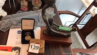 Photo showing the sculpture, NASA medallion in presentation case, wooden music box, and a certificate beneath the medallion.