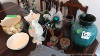 Photo of collection on wooden table including turquoise vase with chip, brown pottery vase, white bird-shaped vase, two decorative bowls, faux flower arrangements, candle, reed diffuser, and blue table runner.