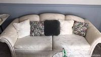 Front view of large beige fabric sofa with cushions showing minor wear and stains.