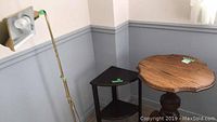 Photo showing the brass-colored floor lamp, dark wood corner table and round wooden pedestal table in a room corner.