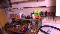 Workbench and shelves with assorted hand and power tools, jars of screws and nuts, as well as sandpaper and other hardware items.
