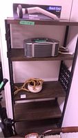 Metal bookcase with four wooden shelves, Panasonic massager box on top shelf, Kaz Ion Generator on second shelf, and hanging planter with rope on third shelf.