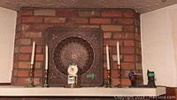 Photo showing 4 brass or copper candle holders (2 pairs, 6 and 8 inches), glass dome covered clock with round dial, screen figure coin banks, and embossed metal tray, all displayed on mantle with brick background.