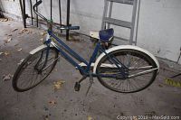 Blue and white vintage ladies bicycle with rear fender, kickstand, and aged paint with rust spots.