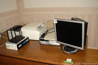 Samsung monitor, scanner, printer, Asus router, keyboard and additional electronics on wooden table against wall.