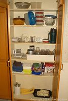 Shelf with glass and plastic storage containers, hand mixers, thermos, measuring cups, and folded kitchen cloths and towels.