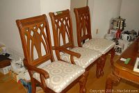 Three chairs positioned side by side showing medium-brown carved wood frames and patterned seat upholstery.