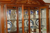 Porcelain dinnerware set for 5 displayed in wooden china cabinet. Plates, cups and saucers feature blue and gold designs on white background.
