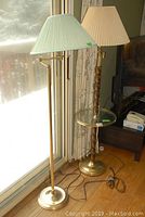 Two vintage floor lamps side by side, one with wood body and glass table, the other brass with adjustable arm and pleated shade, cords visible