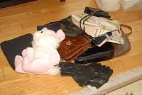 Full view of the pile containing a pink and white stuffed bunny, several handbags, totes, and gloves on a wooden floor.