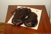 Two brown wigs lying on a white cloth on a wooden table, showing overall condition and color.