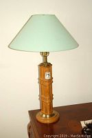 Lamp with wooden base and green lampshade showing stains and brass accents