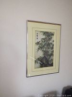 Framed Asian brush painting featuring bamboo and rocks with script, mounted on wall, showing the entire artwork and frame
