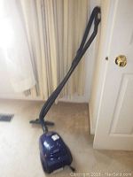 Photo showing the canister part of the blue Bissell Butler vacuum with attached hose and handle, upright position.