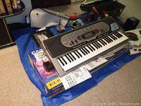 Casio CTK-573 keyboard on original box with manuals on a blue tarp surface surrounded by various items.