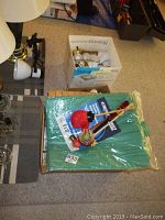 Photo showing the new 9x12 green tarpaulin still sealed in packaging and one box of assorted light bulbs with some bulbs visible on top