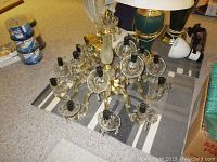 Fifteen light crystal chandelier laid on floor, showing full structure and detailing of arms and crystal components.