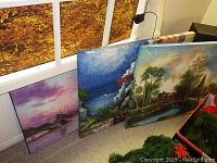 View showing two acrylic landscape paintings and one seascape plaque leaning against a wall, no frames visible.