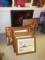 Framed art pieces arranged leaning against a wall showcasing different paintings including floral and landscape themes in various frames.