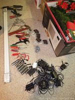 Overview photo showing assortment of hand tools including clamps, wrenches, measuring ruler, caster wheels, a box with Christmas plants, and power adapters with cables