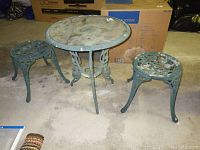 Full view of the patio set showing two cast metal chairs without backs and one glass topped cast metal table.