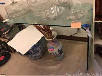 Glass console table shown from front angle with glass dishes on top, clear transparent surface, rounded edges visible.