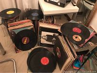 Multiple stacks of vinyl record albums in cardboard storage boxes with loose LPs leaning and scattered on floor