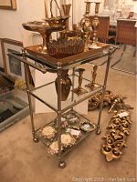 Front angle view of rolling bar cart with metal frame and two glass shelves, holding brass items (not included).