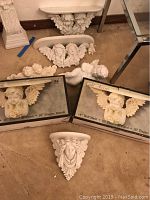Photo showing five cherub wall shelves, two cherub plaques, and one cherub figurine all in white with detailed wings and floral motifs.