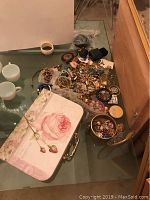 Glass tabletop view showing mixed jewelry pieces and floral suitcase box