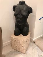 Front view of black composite female torso sculpture mounted on stone pedestal