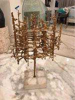 Front view of gilded metal abstract sculpture on square white marble base
