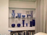 Shelf display of eleven blue glass items including vases, stemware glasses, decorative spheres and bowl in varying blue shades and patterns