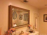 Wall mirror mounted above a sink with gold-colored ornate frame, showing the detailed frame edges and style.