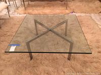 Front view of the glass and metal coffee table showcasing square glass top and metal X-shaped base.