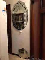 Full view of oval mirror hanging on wall with carved top crest