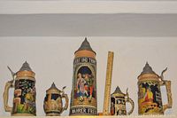 Front view of five German beer steins showing varying sizes and detailed relief decoration with pewter lids.