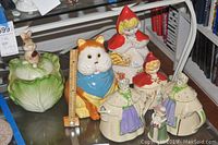 Full view of fairy tale themed ceramic teapots and cookie jars including cabbage bunny, large cat with blue scarf, and Red Riding Hood sets