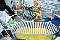 White metal bench with circular seashell design on back and slatted seat, shown from front and side angles.