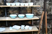 Full shelving display showing 15 Pyrex glass items in blue turquoise color with lids and bowls.