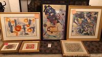 Six framed abstract art pieces arranged on a table, showing the general variety and framing styles.
