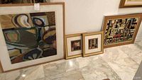 Four framed contemporary abstract art pieces placed leaning against wall. Show variations in size and design.