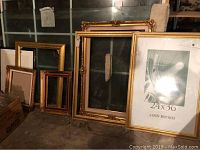 Multiple empty picture frames of assorted sizes leaning against a window and wall, size range approximately 42x31 to 12x14 inches. Frames are decorative, some gold-tone, some wooden.