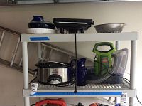Plastic shelving holding a Rival slow cooker, Bissell vacuum, metal colander, blue vase and other items