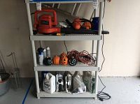 Shelf containing Black and Decker leaf blower, power drill, hedge trimmers, Halloween decorations, extension cords, and lawn chemicals.